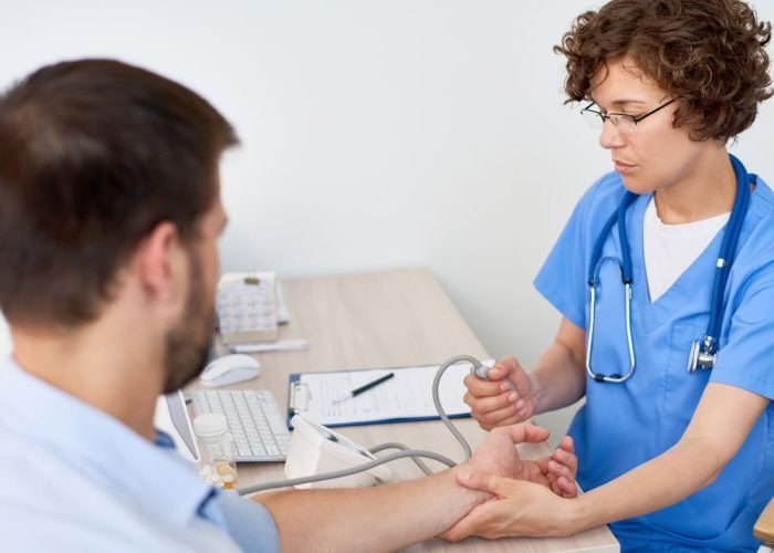 Portrait of young woman measuring patients blood pressure at desk in doctors office